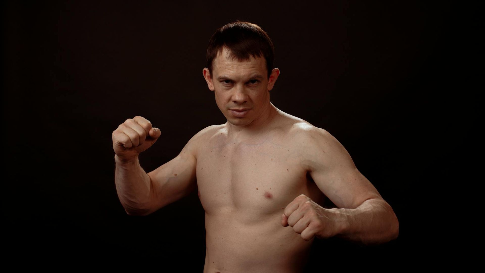 A man in athletic wear standing in a calm, focused stance in a spacious, minimalist studio.